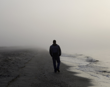 A silhouetted figure walking on a foggy shore.