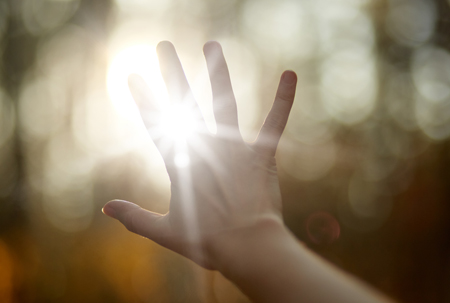 A hand with fingers spread against the shining sun.