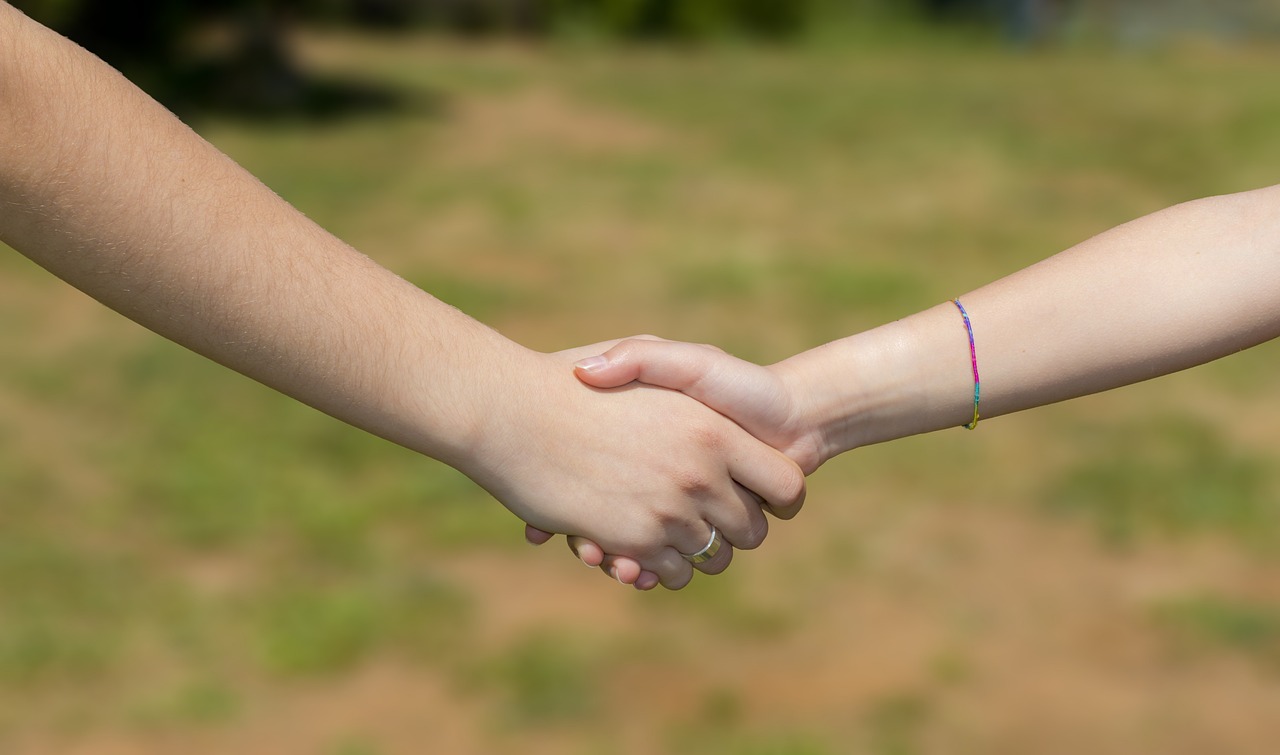Two people grasping hands over a grassy background