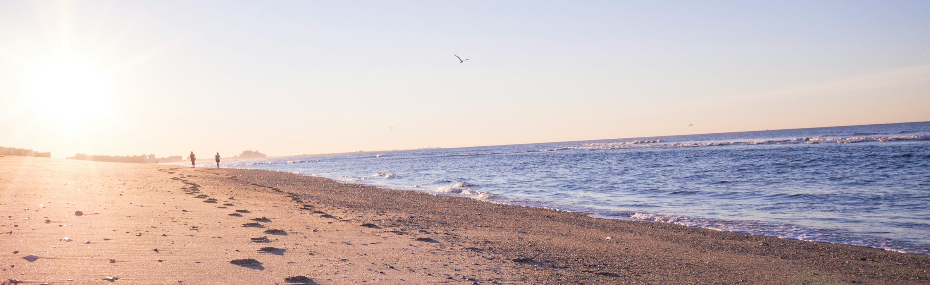 A wide angle shot of a beach horizon in the late afternoon with shadowed figures walking in the distance.