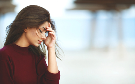 A young woman looking distressed, holding her head in her hand.