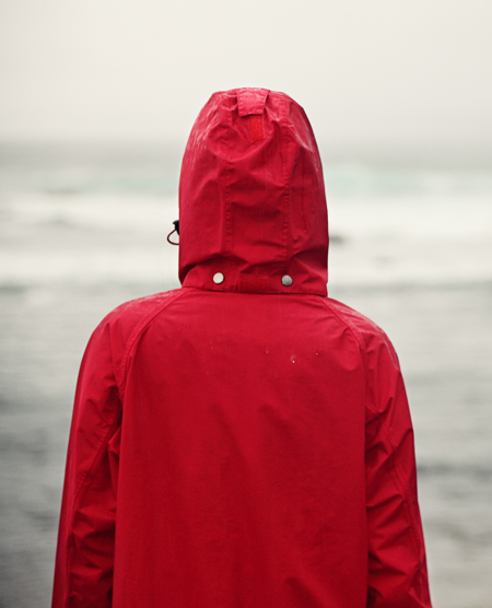 A person stands in a red raincoat, facing away from the camera.