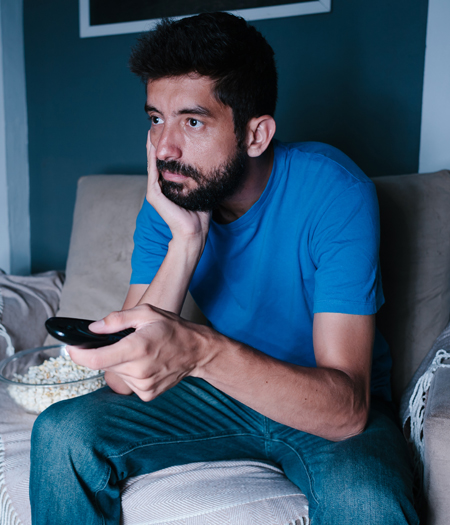 A man looks bored, mindlessly pushing buttons on a tv remote.