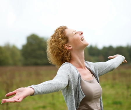 A smiling woman with outstretched arms in a grassy field.