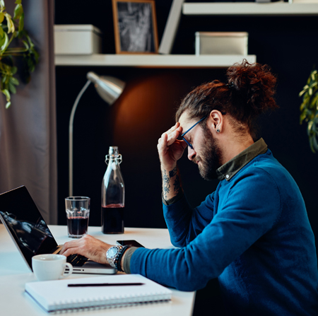 A man sits at a laptop, looking stressed.